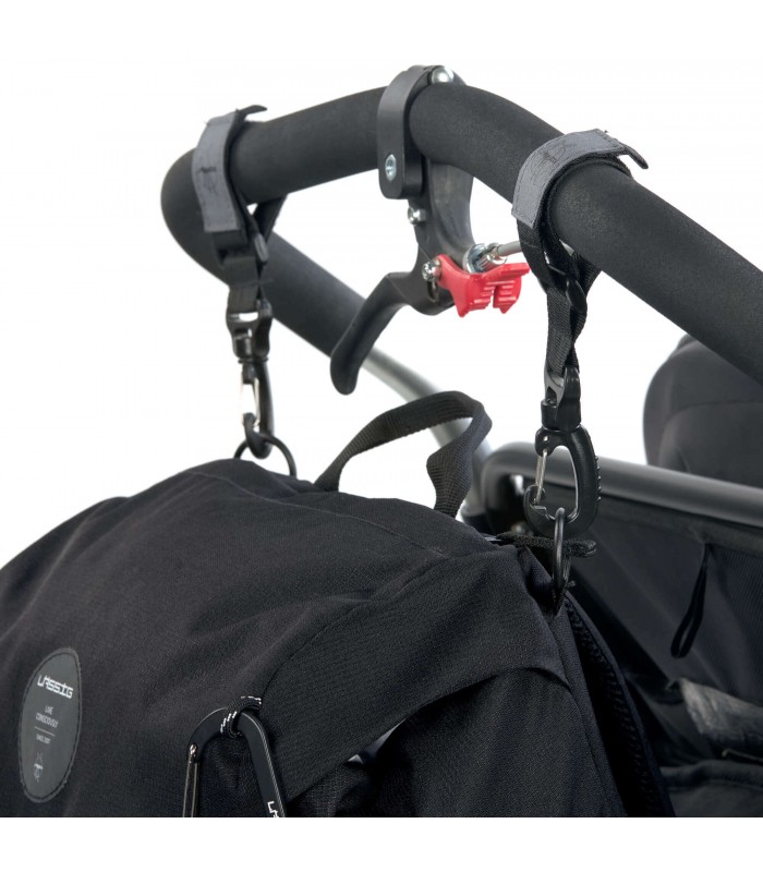 Mochila outdoor Lässig negra de tela resistente, sujeta al manillar de un cochecito con correas y mosquetones negros.