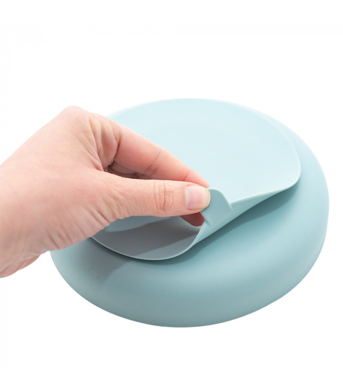 Mano levantando la base de ventosa de un cuenco de silicona azul claro Olmitos, mostrando su flexibilidad y agarre.