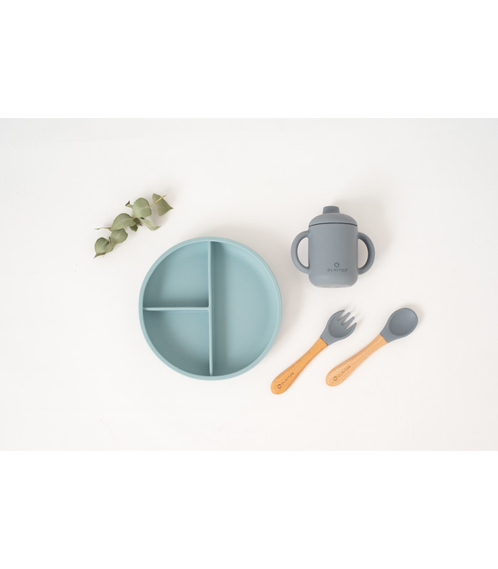 Vajilla de silicona azul y gris con plato dividido, taza con asas y cubiertos con mango de madera sobre fondo blanco.