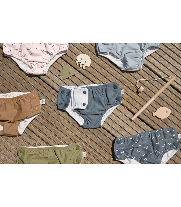 Pañales bañadores Lässig de tela con botones laterales en diversos colores y estampados sobre una superficie de madera.