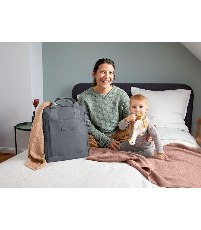 Mochila de pañales Vividal Lässig gris oscuro, de forma rectangular y tela resistente, situada sobre una cama blanca.