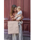Mochila Tyve Lässig beige de forma rectangular y material arrugado, mostrada por una mujer que sostiene a un bebé.