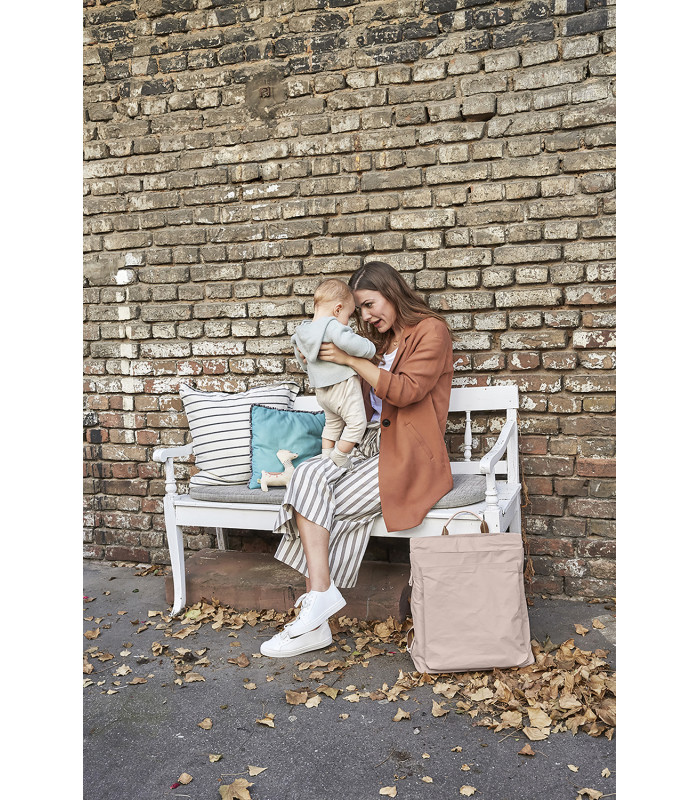 Mochila Tyve Lässig rectangular en color arena y material ligero, situada en el suelo junto a un banco blanco de madera.