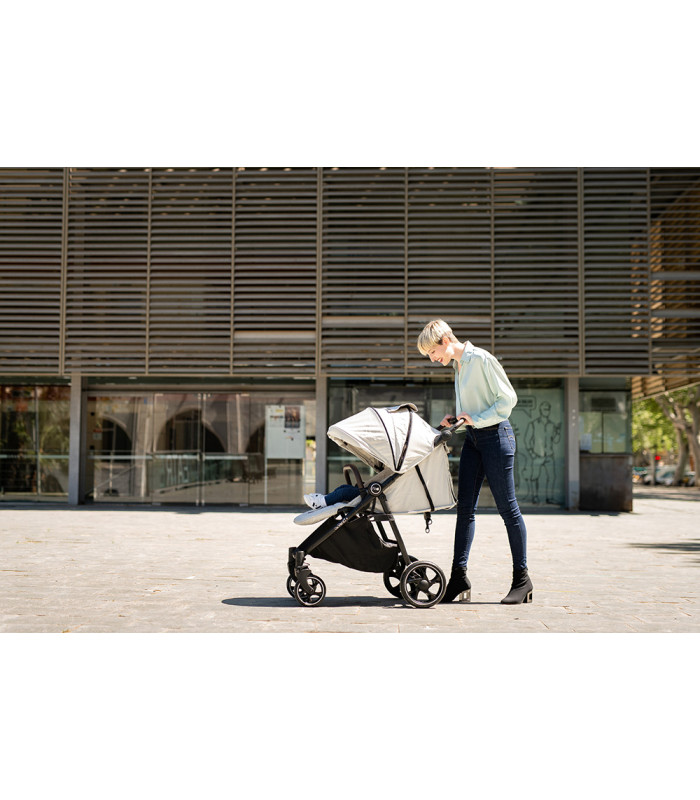 Silla de paseo VentT+ Niu con capota blanca y chasis negro, manejada por una persona en un entorno urbano moderno.