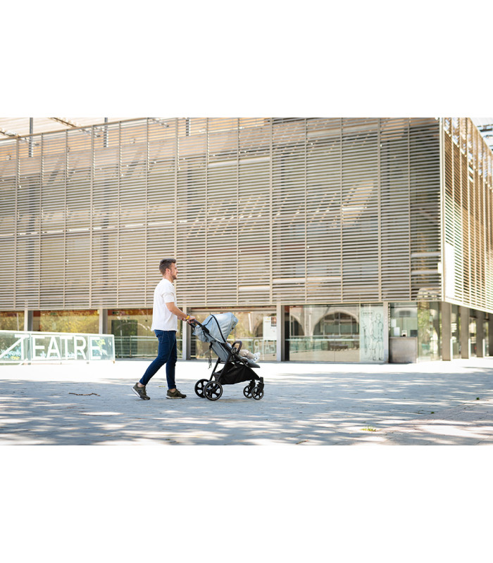 Silla de paseo VentT+ Niu con capota gris y chasis negro, manejada por un hombre frente a un edificio moderno.