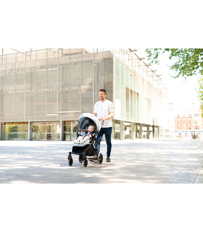 Silla de paseo VentT+ Niu con chasis oscuro y capota gris, empujada por un hombre en una plaza amplia y luminosa.