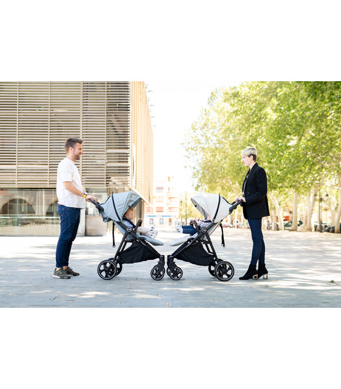 Pareja paseando con dos sillas VentT+ Niu de color gris claro, diseño compacto con chasis negro y ruedas robustas.