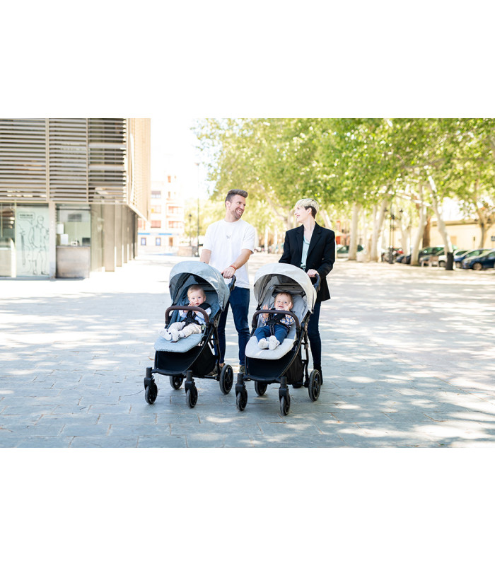 Silla de paseo VentT+ Niu gris con chasis negro y capota extendida, usada por una pareja en una calle soleada con árboles.