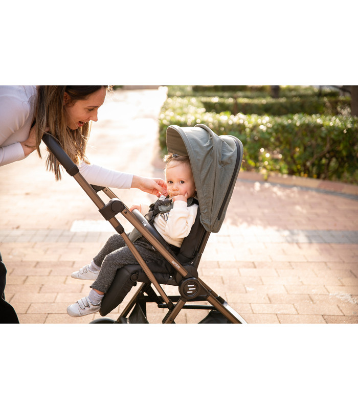 Silla de paseo Eolia Niu en color gris con chasis negro. Una madre sonríe a su bebé sentado en el cochecito al aire libre.
