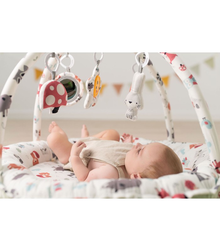 Alfombra de juegos Olmitos blanca con estampados, bordes elevados y arcos con juguetes como una seta y un espejo.