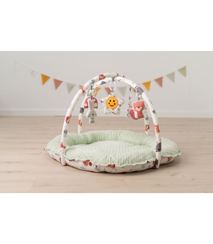 Gimnasio Olmitos con base redonda acolchada verde menta, arcos blancos cruzados y coloridos juguetes colgantes.