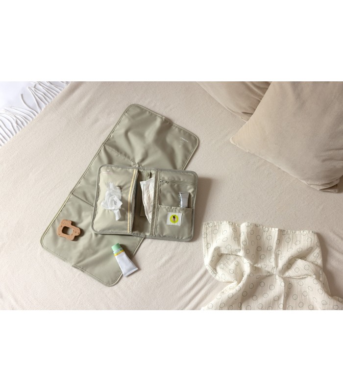 Cambiador portátil Lässig verde salvia de tela, con compartimentos para pañales, abierto sobre una superficie clara.